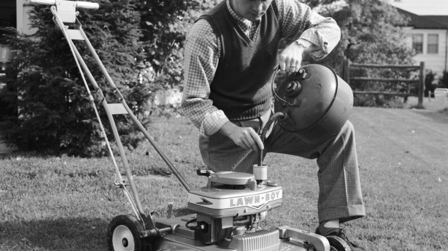 A black and white photo of a man mixing oil and gasoline to use his Lawn-Boy push mower model