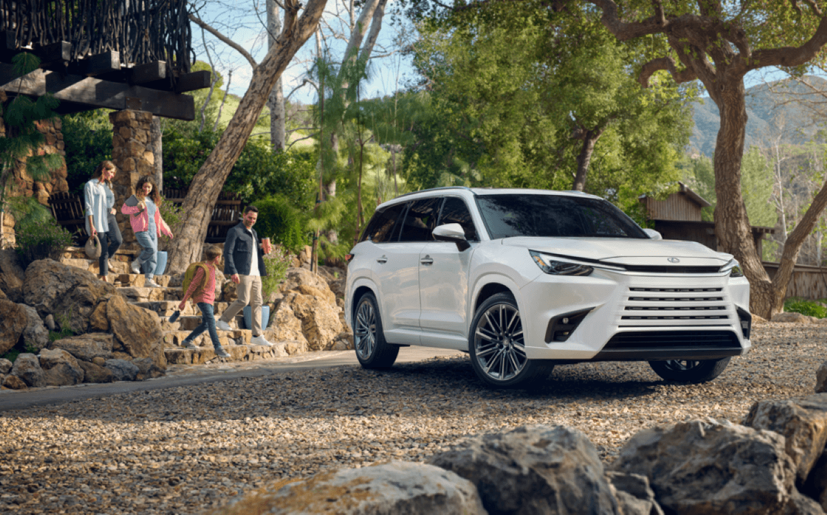 A family walking down stone stairs toward a 2024 Lexus TX Premium full-size luxury SUV model parked on gravel