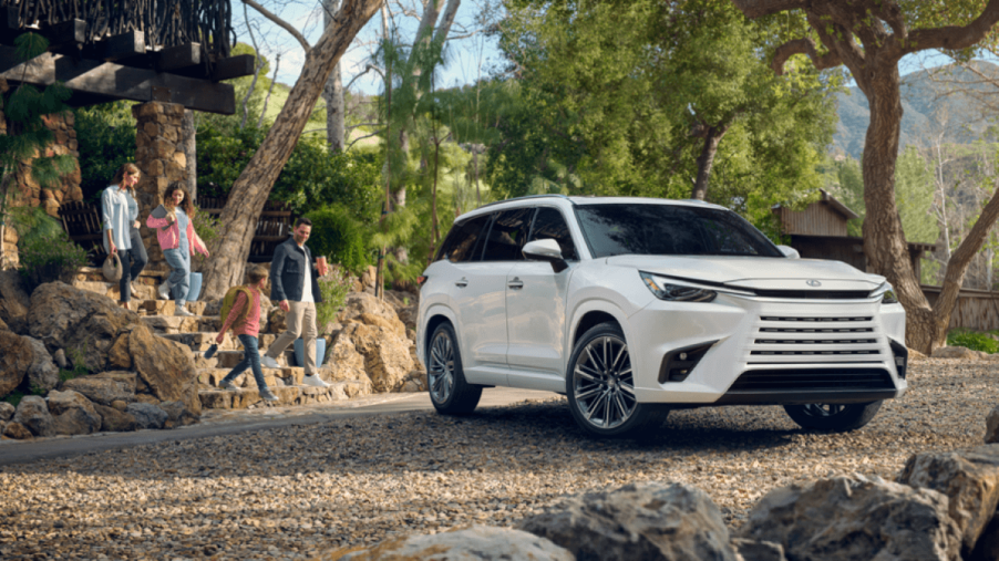 A family walking down stone stairs toward a 2024 Lexus TX Premium full-size luxury SUV model parked on gravel