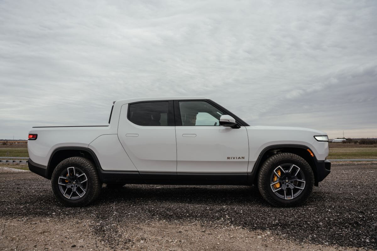 A side profile exterior shot of a Rivian R1T all-electric truck outside a manufacturing plant in Normal, Illinois