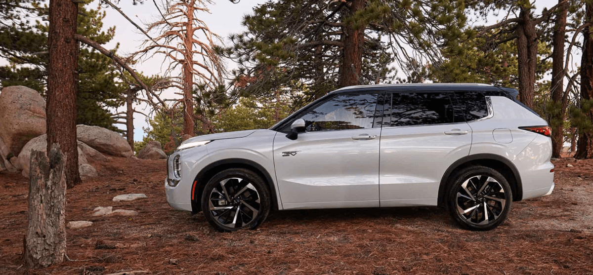 A side profile shot of a 2024 Mitsubishi Outlander PHEV compact SUV model parked on brush in a forest