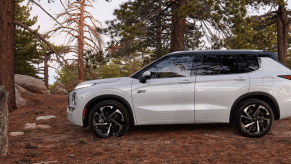 A side profile shot of a 2024 Mitsubishi Outlander PHEV compact SUV model parked on brush in a forest