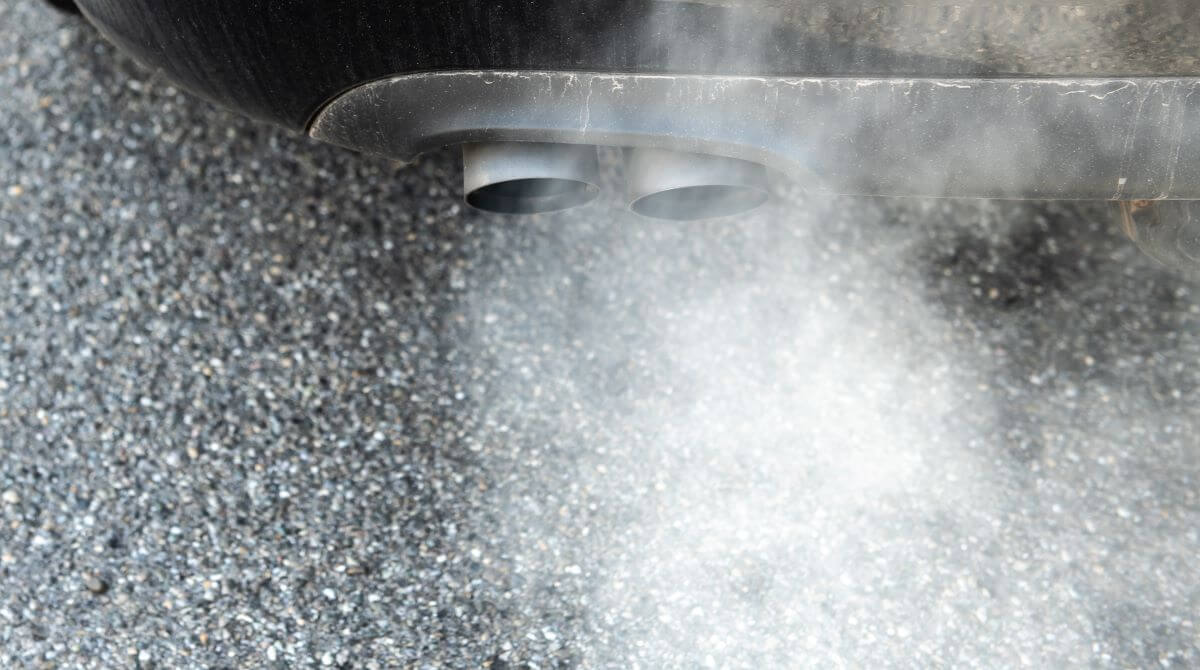 A diesel vehicle spewing out white smoke from its exhaust system while parked on asphalt