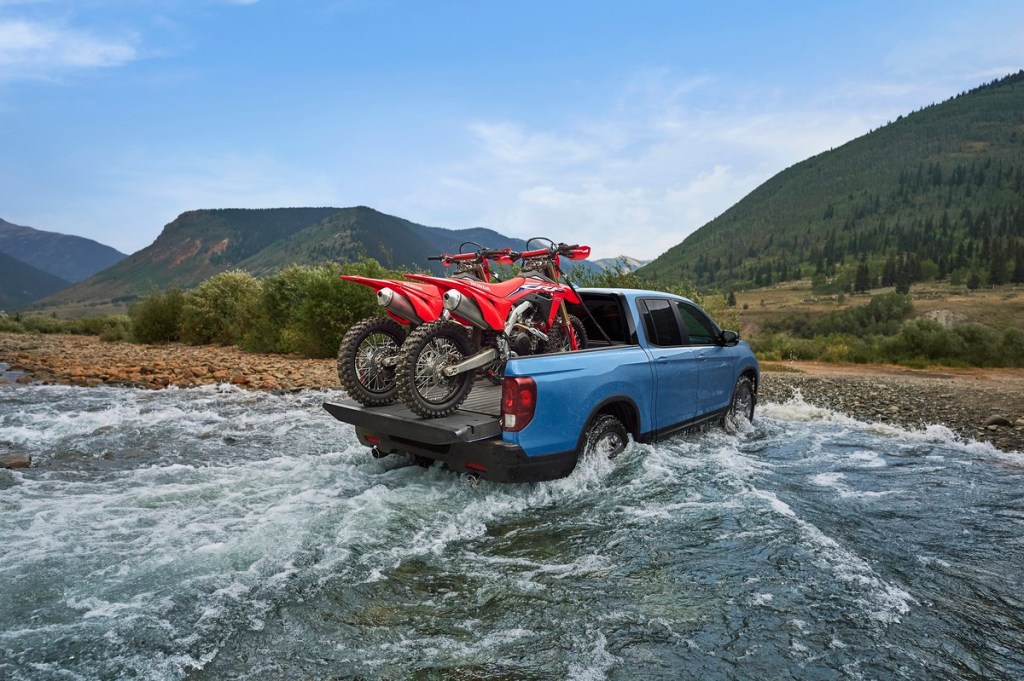 2024 Honda Ridgeline TrailSport crossing a river with two dirt bikes in the back