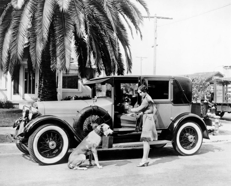 Black and white photo of a woman getting into a 1920s Lincoln, beneath a palm tree.