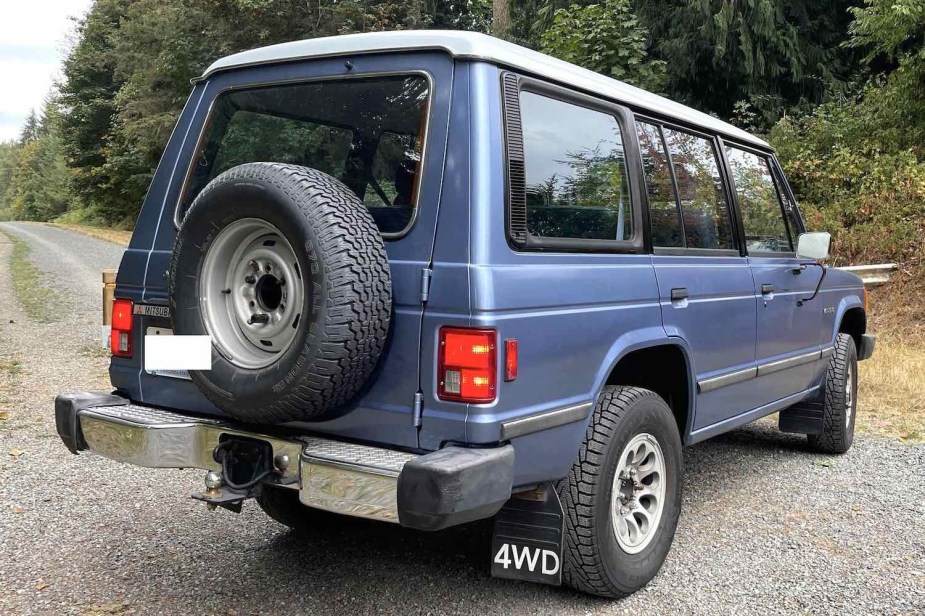 Blue first-gen Mitsubishi Montero four-door SUV with a white top, trees visible in the background.