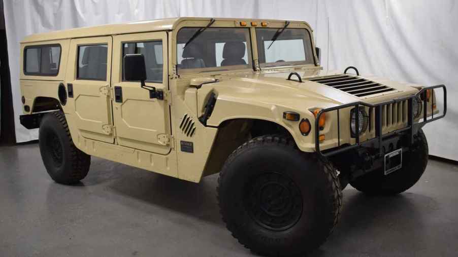 A desert tan 1992 Hummer H1 Humvee parked at right front angle in front of a white curtain