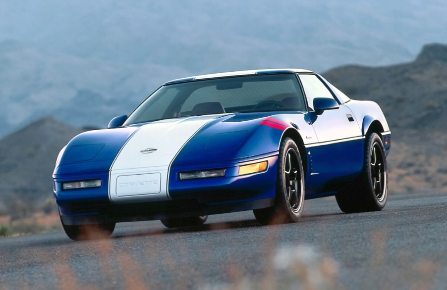 A blue and white C4 Corvette Grand Sport from the 1996 model year drives around a corner.