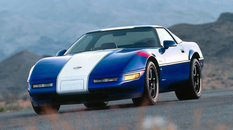 A blue and white C4 Corvette Grand Sport from the 1996 model year drives around a corner.