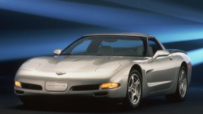 A silver Chevrolet C5 Corvette sits on a stage next to a blue backdrop.