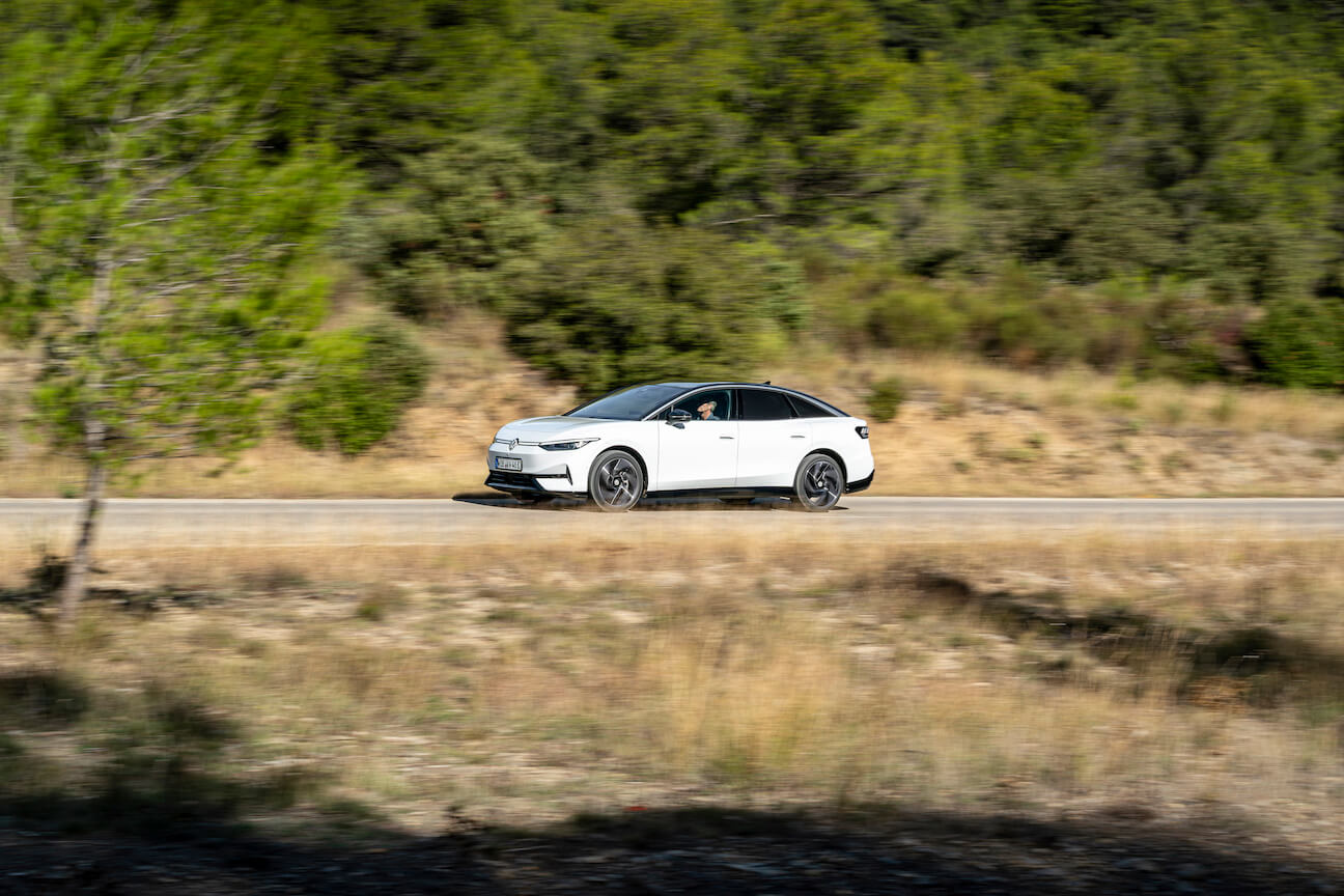 A white Volkswagen ID.7 driving on a desert road with some shrubbery in the background.