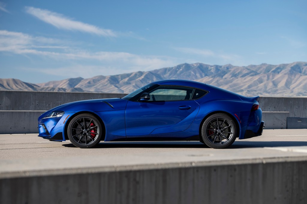 A blue 2023 Toyota Supra is shown in full left side view parked on a highway with a mountain in the background