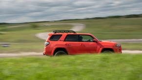 An orange 2023 Toyota 4Runner TRD Pro is shown driving in the midground with grass in the foreground