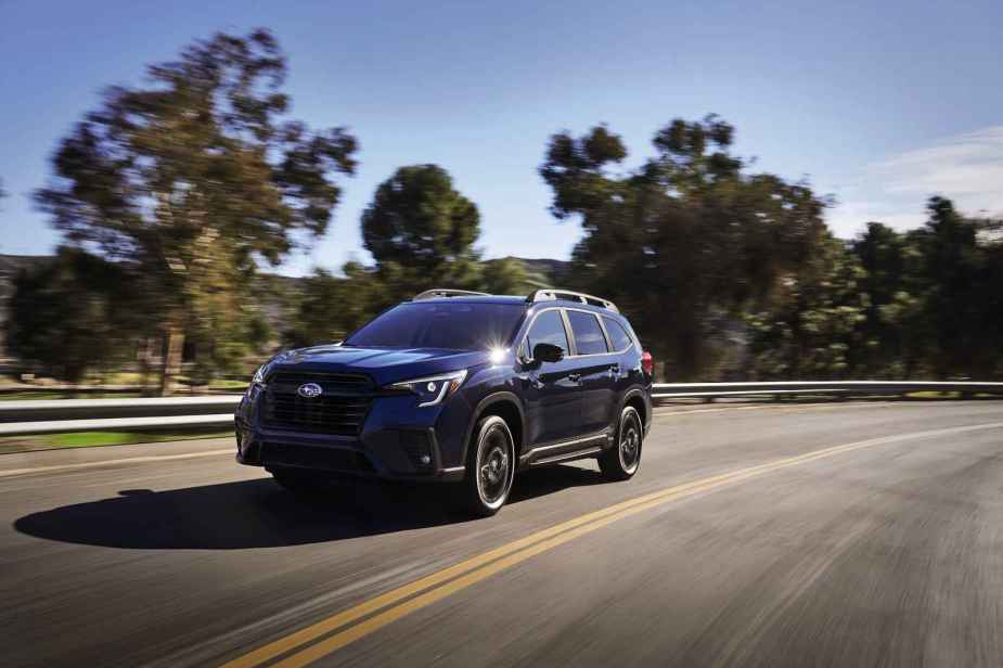 A dark-colored 2023 Subaru Ascent shown driving on a two-lane road with trees in the background