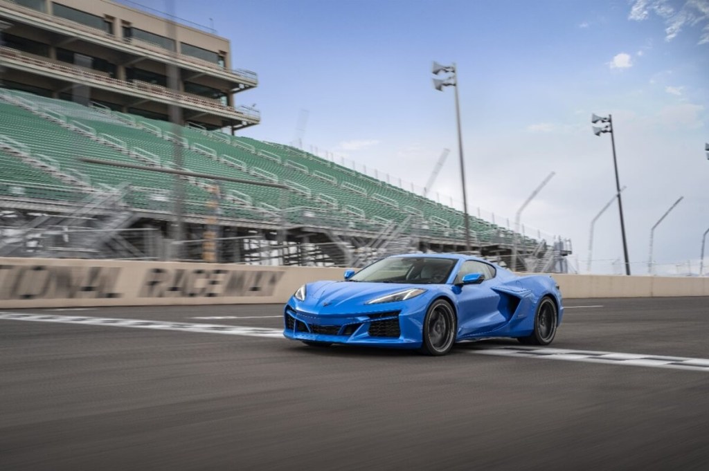 A blue 2024 Corvette E-Ray drives across the line at a track.