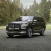A black full-size SUV, the 2024 Lincoln Navigator, is parked outside surrounded by trees.