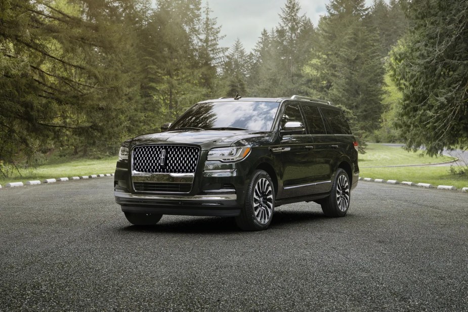 A black full-size SUV, the 2024 Lincoln Navigator, is parked outside surrounded by trees.