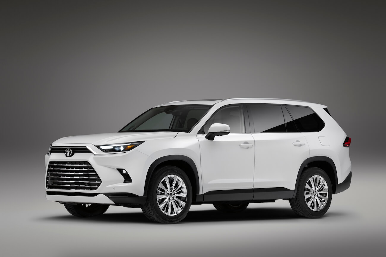 A white Toyota Grand Highlander against a white/gray backdrop display. 2024 Toyota Grand Highlander sales are growing.