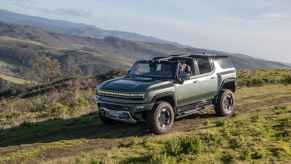 A 2024 GMC Hummer EV SUV is shown driving down a grassy mountainous incline with top open