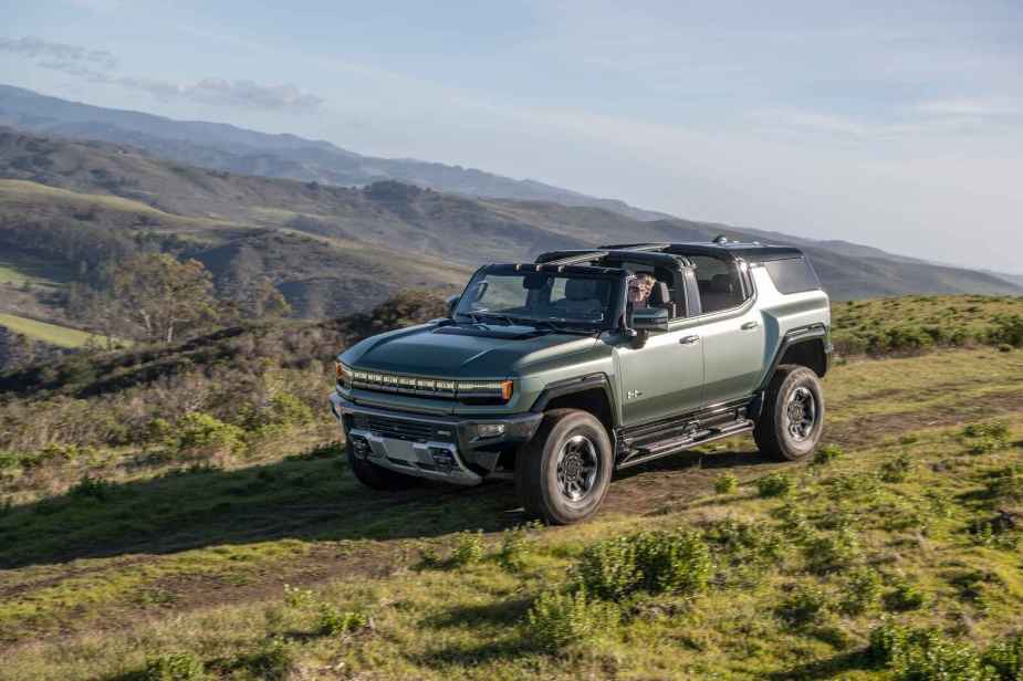 A 2024 GMC Hummer EV SUV is shown driving down a grassy mountainous incline with top open