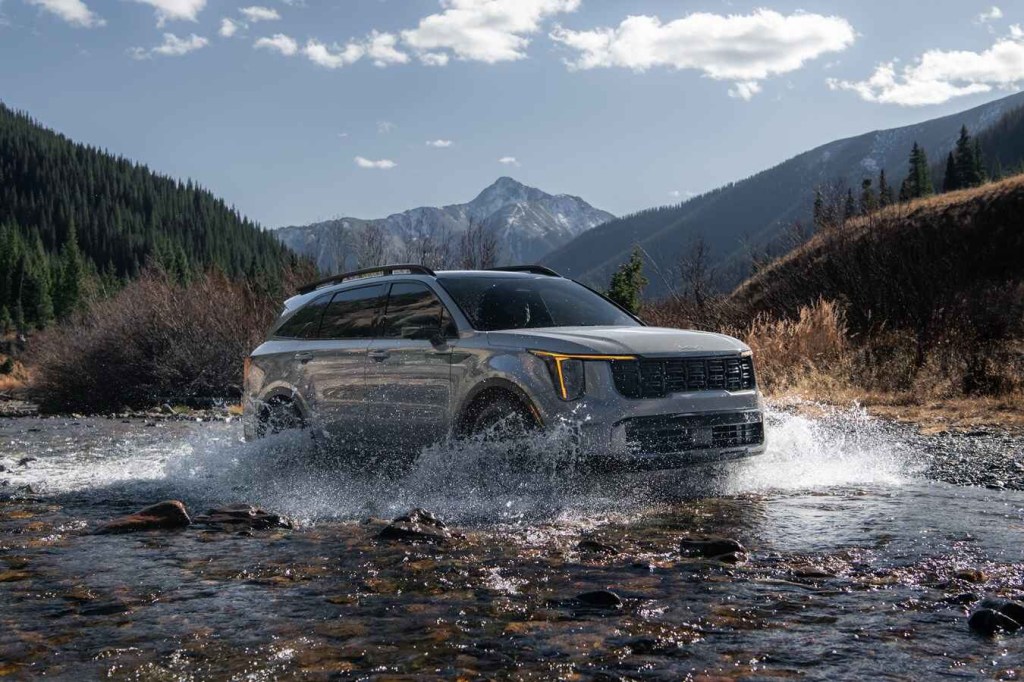 A grey 2024 Kia Sorento drives across a rapid creek with a mountain in the background
