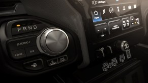 The shift knob of a Ram 1500 REV "Ramcharger" configuration with its V6 rang-extender status visible in the background.