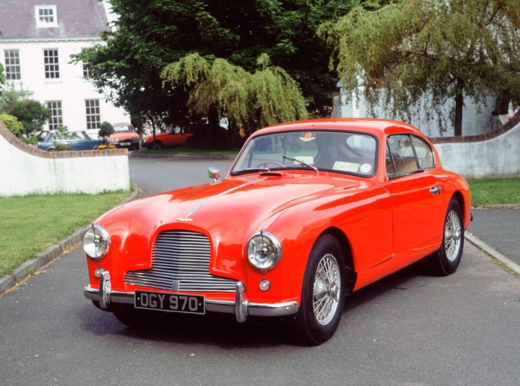 An Aston Martin DB2-4 shows off its classic car looks beside a large home.