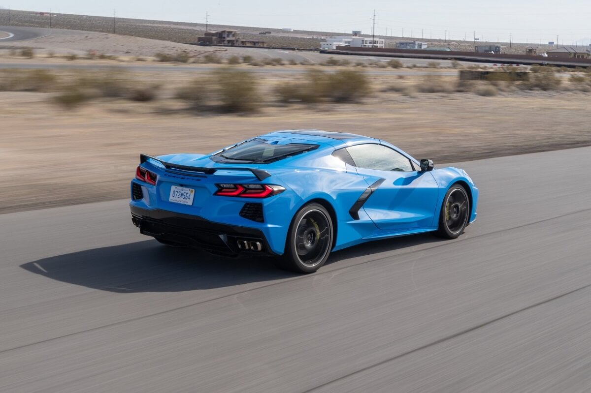 A blue C8 Chevrolet Corvette Stingray cruises down a track in the desert.