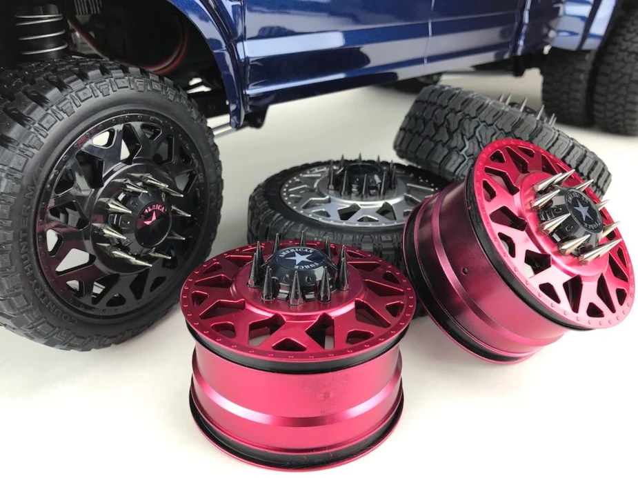 Aftermarket rims with spiked lug nuts stacked next to a Ford F-150 pickup truck.