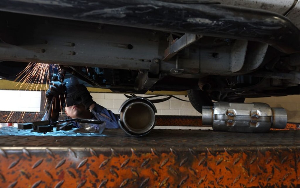 A tech works on a vehicle beside a catalytic converter to prevent it from being stolen. 