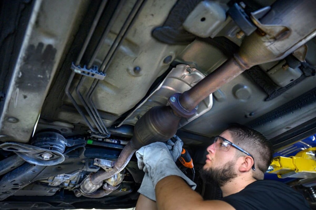 A tech adds a license plate number to a vehicle's catalytic converter to prevent theft and price of replacement.