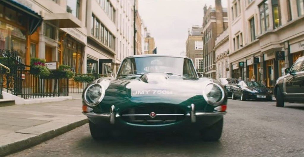 A green Jaguar E-Type movie car pulls up onto a London street. 
