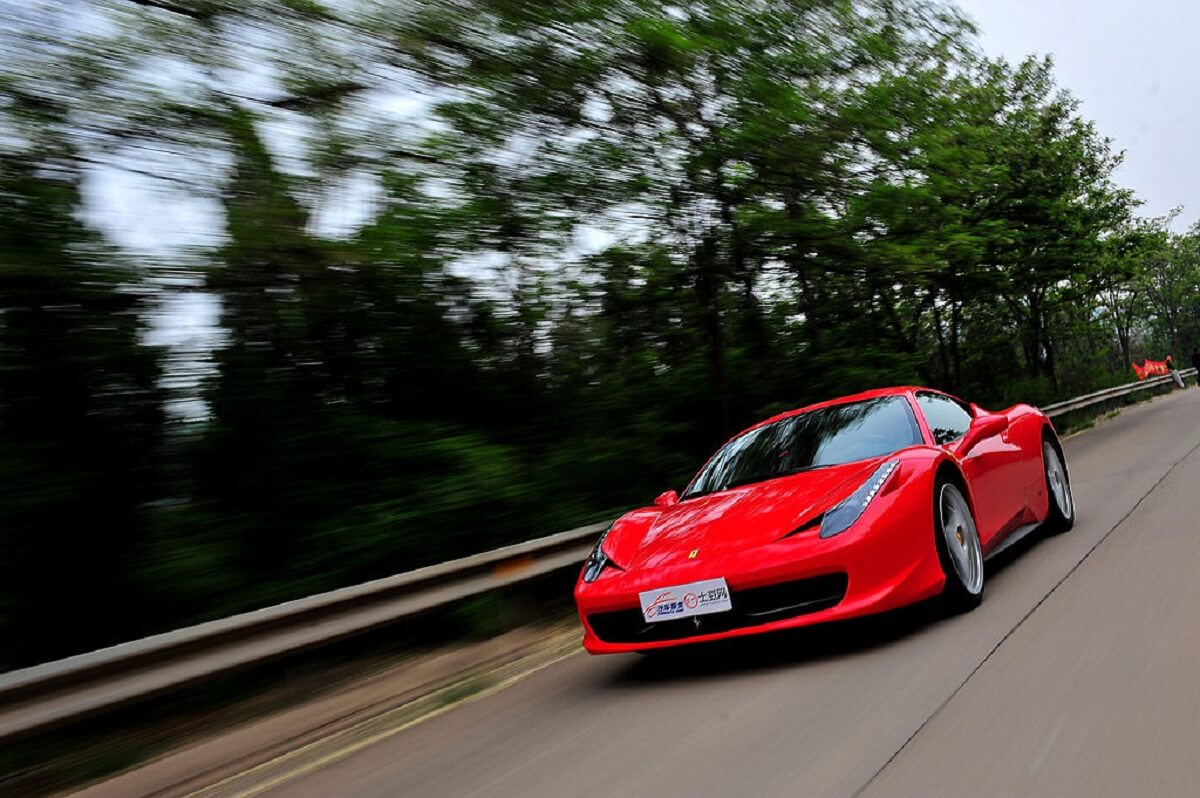A red Ferrari 458 Italia blasts down a forest road.