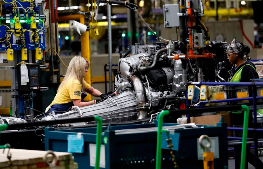 Two workers assemble the engine and transmission of a heavy duty GMC diesel pickup truck in Flint, Michigan.