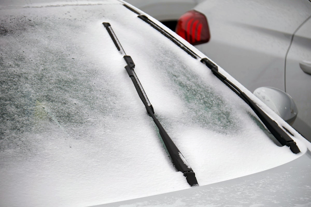 Snow covers a frozen car windshield and wipers
