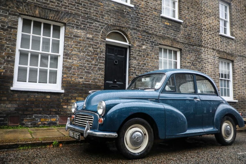 A blue Morris Minor economy car, like Rowan Atkinson's, is far from a celebrity car, but looks at home next to an old building.