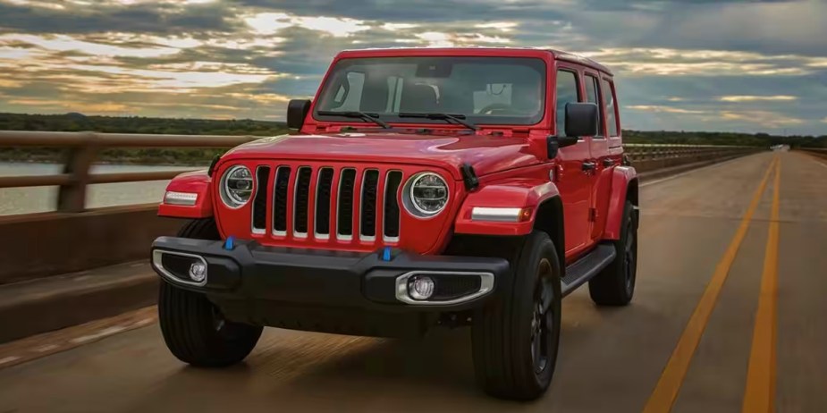 A red Jeep Wrangler 4xe plug-in hybrid small plug-in hybrid SUV is driving on the road. 
