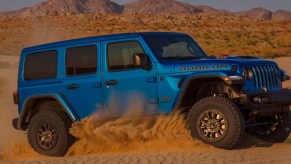 A blue Jeep Wrangler 4xe small plug-in hybrid SUV is driving off-road.