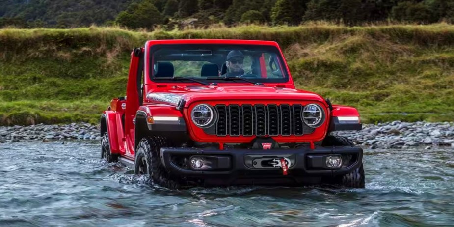 A red Jeep Wrangler small SUV is wading through water. 