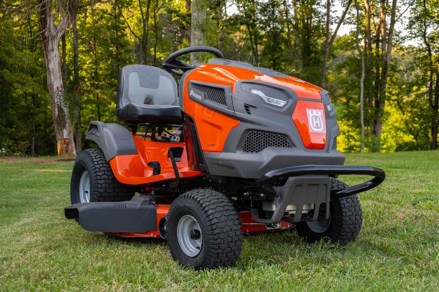 An orange lawn tractor parked in front of a row of trees.