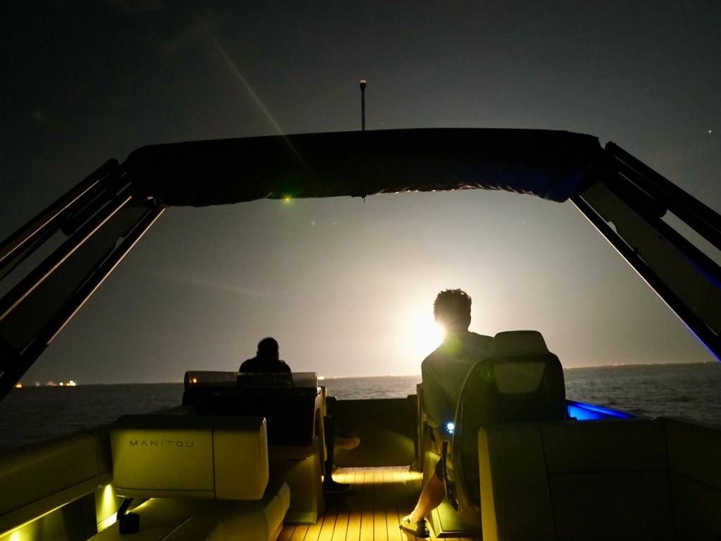 A Falcon 9 rocket launch lights up the sky as seen from a Manitou pontoon boat.