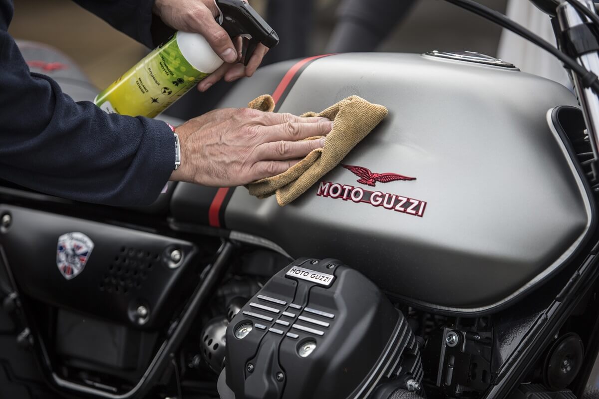 A rider polishes a Moto Guzzi V7 cafe racer motorcycle.