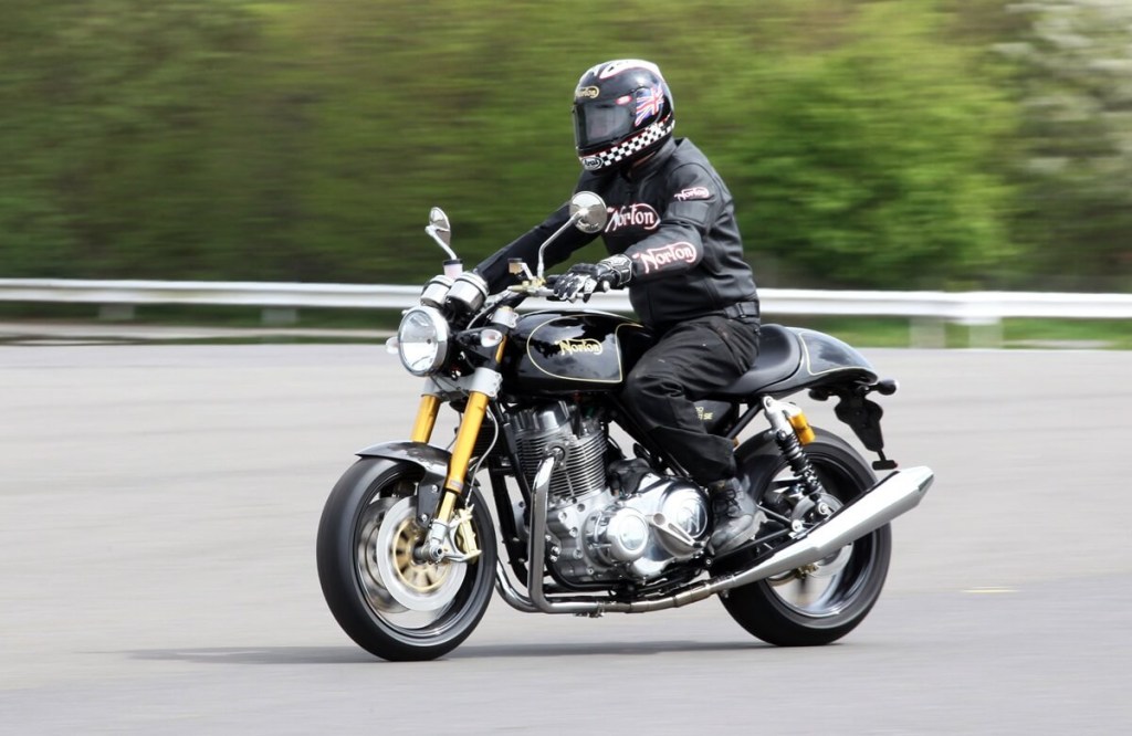 A rider cruises on a Norton Commando 961SE cafe racer motorcycle.