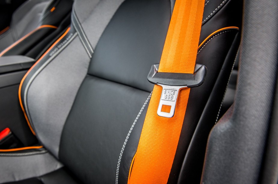 Bright orange seat belt, unbuckled on a leather truck seat.