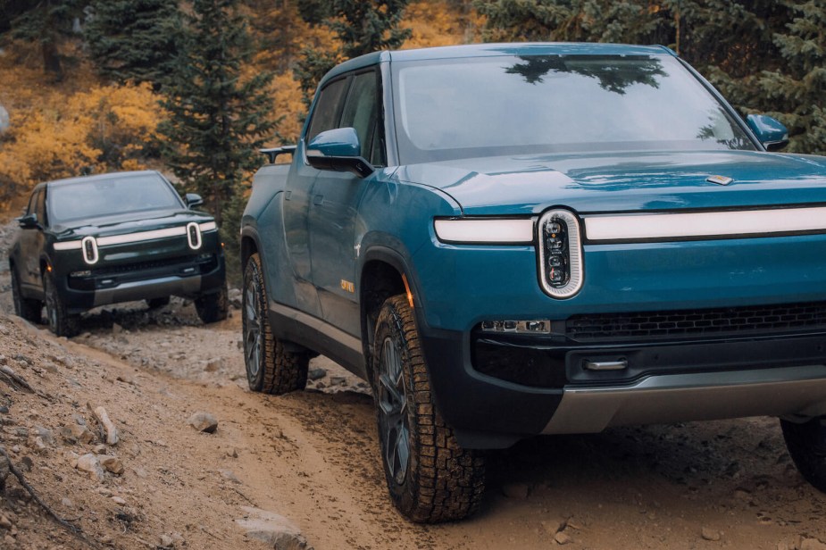 Blue and black electric Rivian pickup trucks climbing an off-road trail.