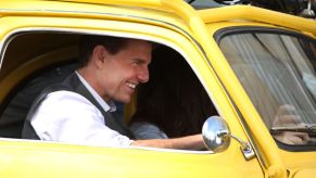 Tom Cruise, a famous movie star and celebrity, sits in a classic car on set of a movie.
