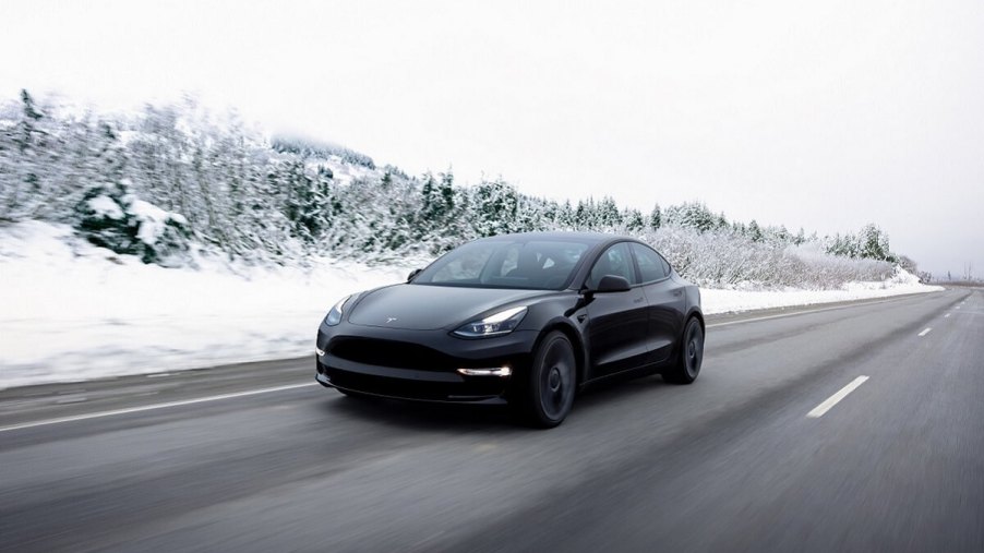 A black 2023 Tesla Model 3 electric car drives across a snowy landscape.