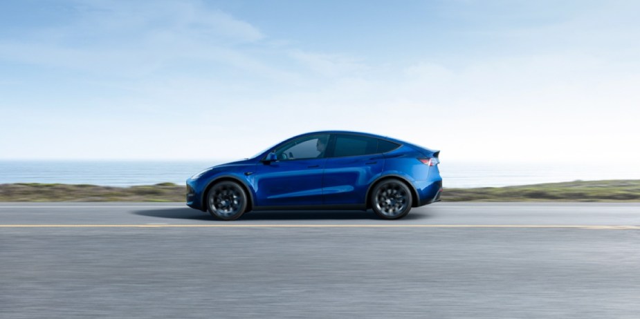 A blue Tesla Model Y small electric SUV is driving on the road. 