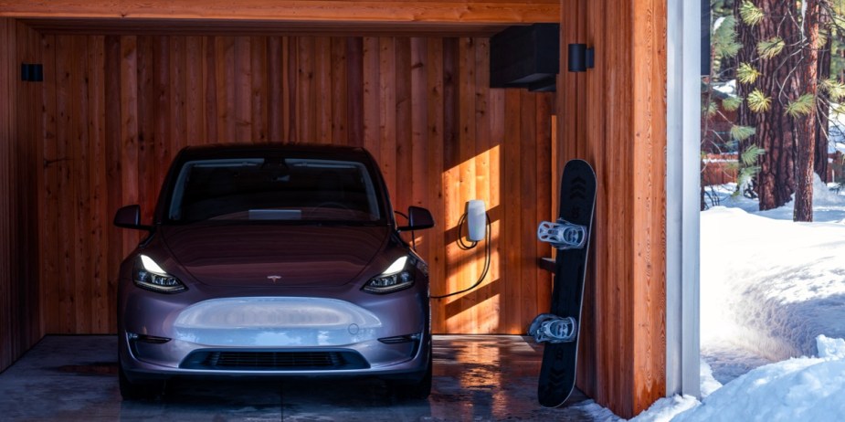 A gray Tesla Model Y small electric SUV is parked in a garage in a snowy area. 