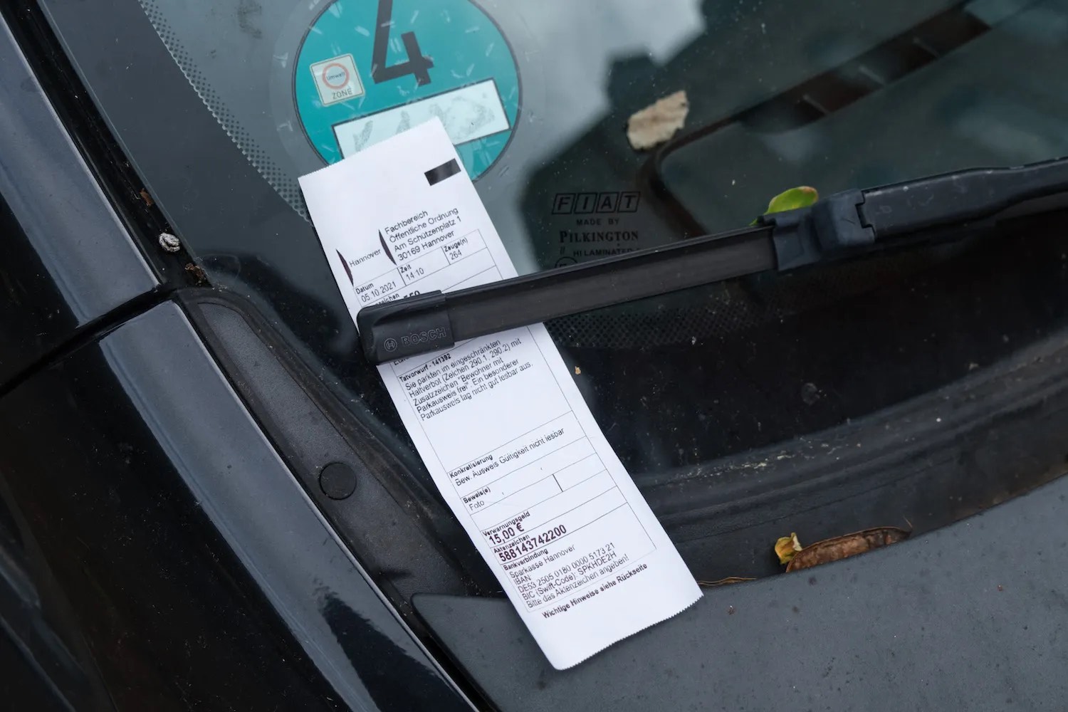 Unpaid parking ticket beneath a windshield wiper.